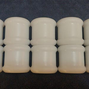May include: A collection of ten white, cylindrical objects arranged in two rows of five. Each object has a rounded top and bottom with a slightly narrower midsection. The objects appear to be made of a smooth, solid material.