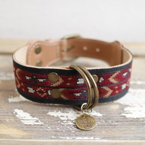 Op de afbeelding: Een rode, zwarte en crèmekleurige hondenriem met een messing gesp en twee messing D-ringen. De riem heeft een messing label met een pootprint.