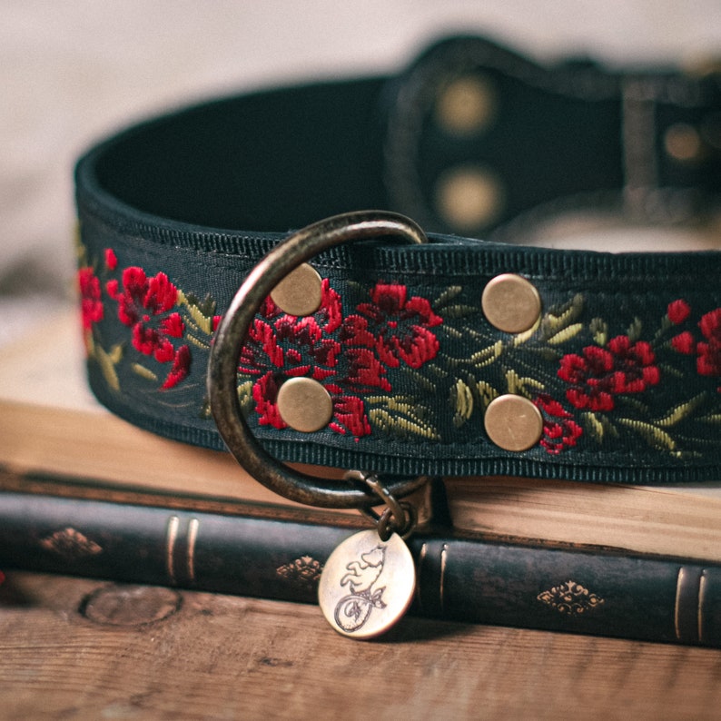 K&ouml;nnte beinhalten: Schwarzes Hundehalsband mit roter Blumenstickerei und goldenen Akzenten. Das Halsband hat ein dekoratives Metalletikett mit einem kleinen Tiermotiv.