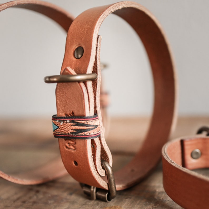 Puede incluir: Dos collares de perro de cuero, uno con una correa de cuero marr&oacute;n y una banda estampada de colores, y el otro con una correa de cuero marr&oacute;n lisa.