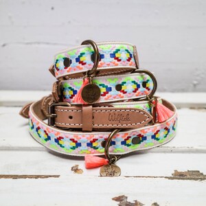 May include: A stack of three colorful dog collars with a white background and a pink tassel. The collars are decorated with a geometric pattern and the top collar has a brass tag that says "Wolfish".
