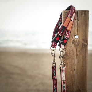 Puede incluir: Dos correas para perros con estampado rojo, blanco y negro con cierres plateados colgando de un poste de madera.