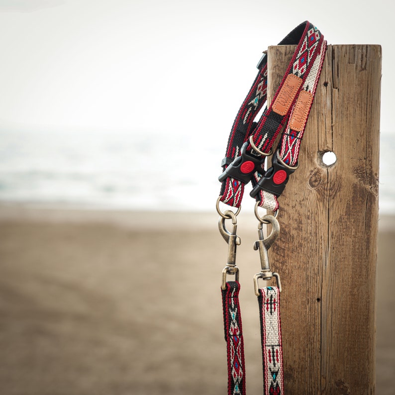Puede incluir: Dos correas para perros con estampado rojo, blanco y negro con cierres plateados colgando de un poste de madera.