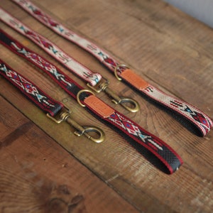 Puede incluir: Tres correas para perros con diferentes patrones. Las correas son negras con dise&ntilde;os geom&eacute;tricos rojos, blancos y azules. Cada correa tiene un gancho de lat&oacute;n y una etiqueta de cuero marr&oacute;n con la palabra "Wander" impresa.