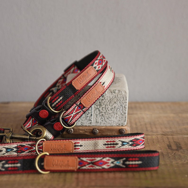 Puede incluir: Dos collares para perros con estampado rojo, negro y blanco con etiquetas de nombre de cuero marr&oacute;n que dicen "Willoh". Los collares est&aacute;n apilados uno encima del otro con una correa a juego en primer plano.