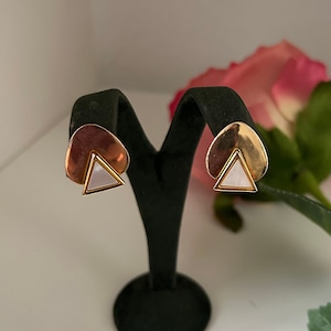 May include: A pair of gold tone earrings with a white triangle shaped stone in the centre. The earrings are on a black display stand.