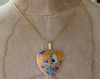 May include: A gold chain necklace with a heart-shaped pendant. The pendant is decorated with a butterfly and floral design in shades of blue, yellow, and red.