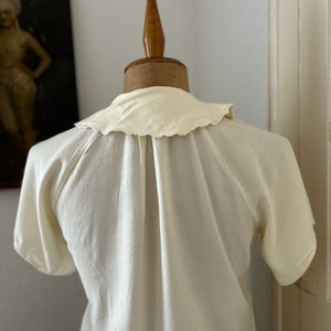 May include: A white, short-sleeved blouse with a scalloped collar. The blouse is on a white mannequin.