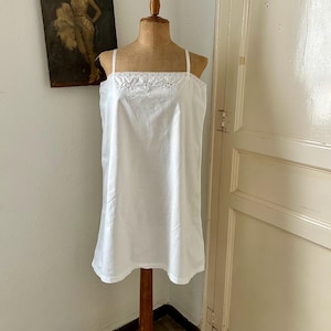 Puede incluir: Una camisa sin mangas de color blanco con tirantes finos y escote cuadrado. La zona superior del pecho está adornada con un delicado borde de encaje blanco y un intrincado bordado floral, lo que le confiere un aspecto limpio y sencillo.