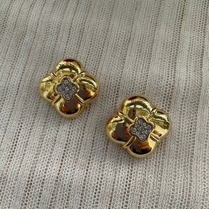 May include: A pair of gold tone earrings with a four-leaf clover design. Each clover has a center of clear rhinestones.