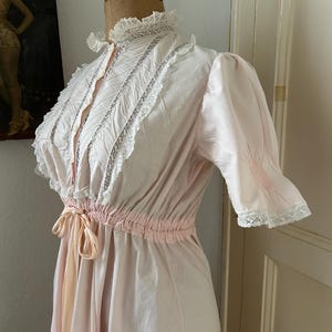 K&ouml;nnte beinhalten: Ein rosafarbenes Vintage-Nachthemd mit wei&szlig;en Spitzenbesatz und einer Schleife an der Taille.
