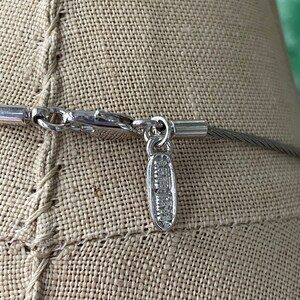 May include: Silver necklace with a silver clasp and a small silver tag that says "Swarovski" on it.