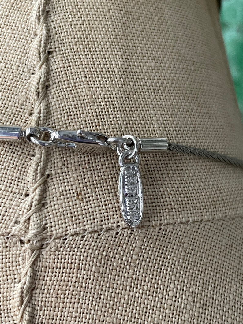 May include: Silver necklace with a silver clasp and a small silver tag that says "Swarovski" on it.