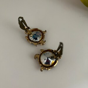 K&ouml;nnte beinhalten: Ein Paar Vintage-Ohrclips. Jeder Ohrring hat einen gro&szlig;en, klaren, facettierten Kristallstein, der in einen goldfarbenen Metallrahmen gefasst ist. Der Rahmen hat einen dekorativen, gewellten Rand und einen Clip-Mechanismus.