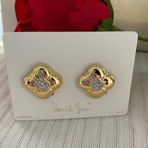 May include: Gold tone earrings with a four-leaf clover design and clear rhinestones. The earrings are on a white card with the text "David Grau" and "Barcelona" printed on it.