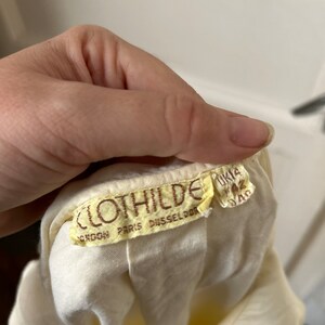 May include: A white cotton dress with a brown label that reads "Clothilde London Paris Dusseldorf" and "UK 12 34D".
