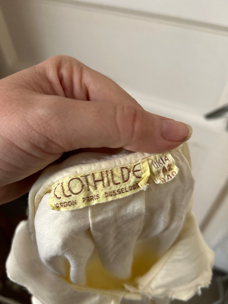 May include: A white cotton dress with a brown label that reads "Clothilde London Paris Dusseldorf" and "UK 12 34D".