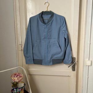 Peut inclure: Une veste bomber bleu clair avec une fermeture éclair et des poignets et une ceinture côtelés.