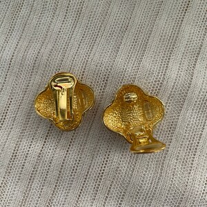 May include: A pair of gold-tone clip-on earrings with a textured, flower-shaped design.