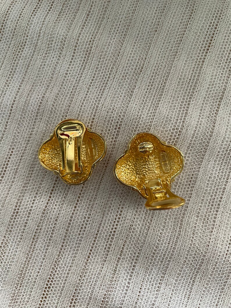 May include: A pair of gold-tone clip-on earrings with a textured, flower-shaped design.