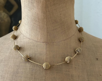 May include: A gold-toned necklace with spiral-shaped beads strung on a delicate chain. The necklace is displayed on a mannequin, showcasing its design and texture. The beads have a natural, earthy color, adding a touch of elegance to the jewelry.