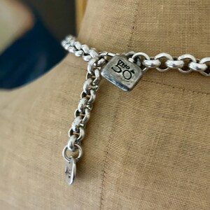 May include: Silver-toned necklace with a chunky chain design. The necklace features a square pendant with the number "50" engraved on it. The necklace is displayed on a mannequin.