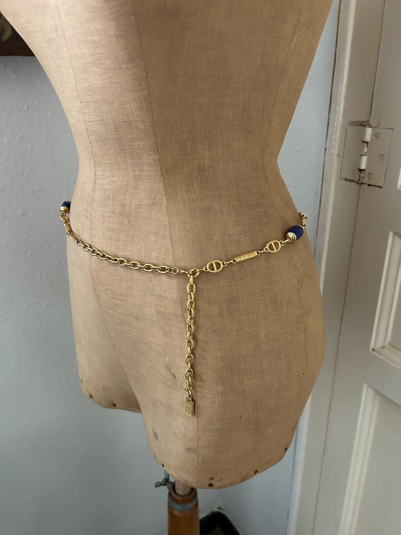 May include: A gold chain belt with blue oval-shaped beads. The chain has a small gold tag hanging from it.