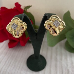 May include: A pair of gold-tone earrings with a four-leaf clover design. Each earring features a cluster of clear rhinestones in the center.