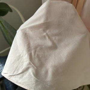 K&ouml;nnte beinhalten: Nahaufnahme eines blassrosa Stoffes mit glatter Textur. Der Stoff ist gefaltet und hat einen dezenten Glanz.