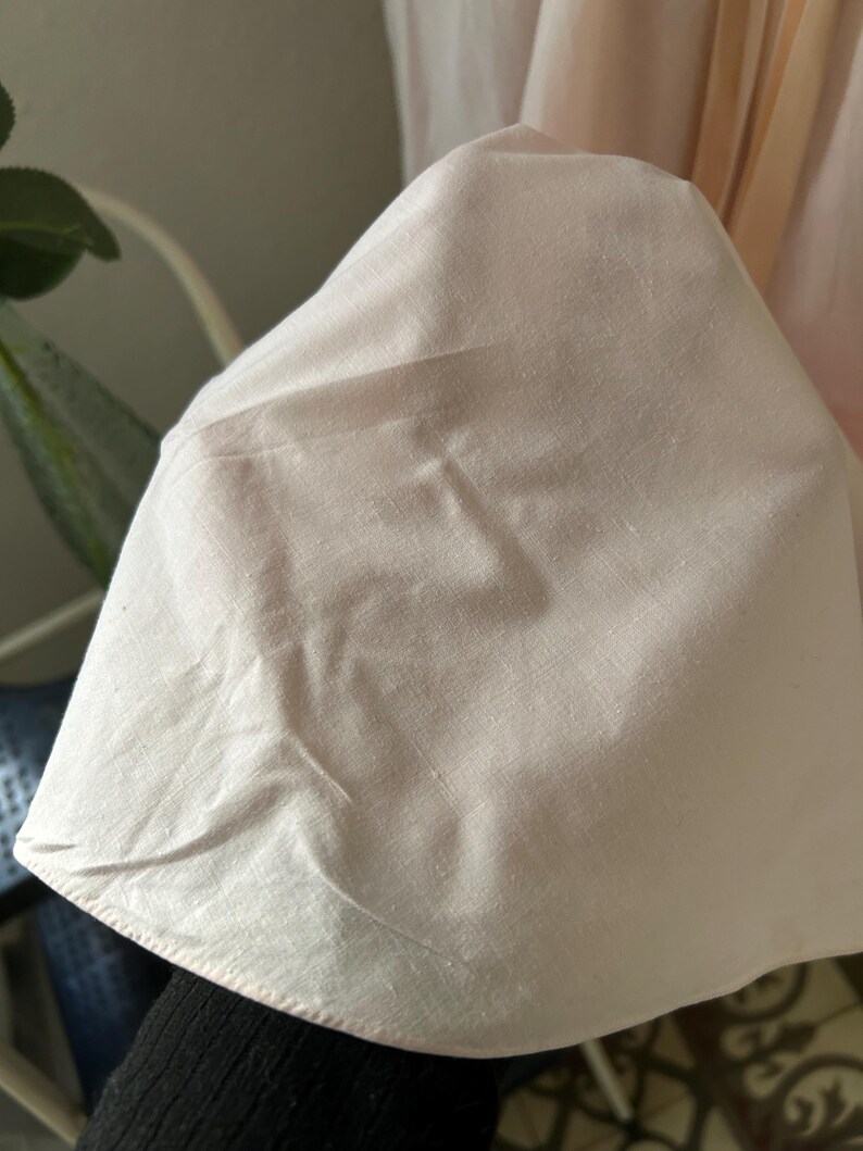 K&ouml;nnte beinhalten: Nahaufnahme eines blassrosa Stoffes mit glatter Textur. Der Stoff ist gefaltet und hat einen dezenten Glanz.
