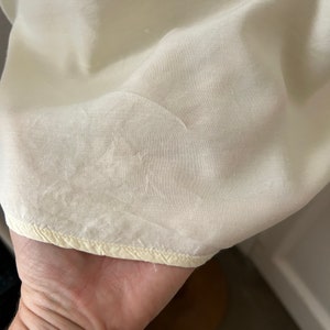 May include: Close-up of a cream-coloured fabric with a subtle texture. The fabric has a yellowed edge with a stitched seam.