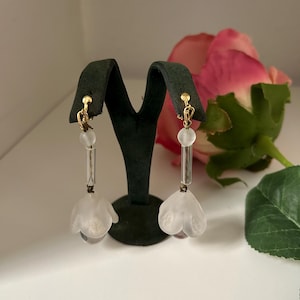 Può includere: Un paio di orecchini pendenti a forma di fiore bianco con perline di vetro trasparenti e dettagli in metallo dorato.