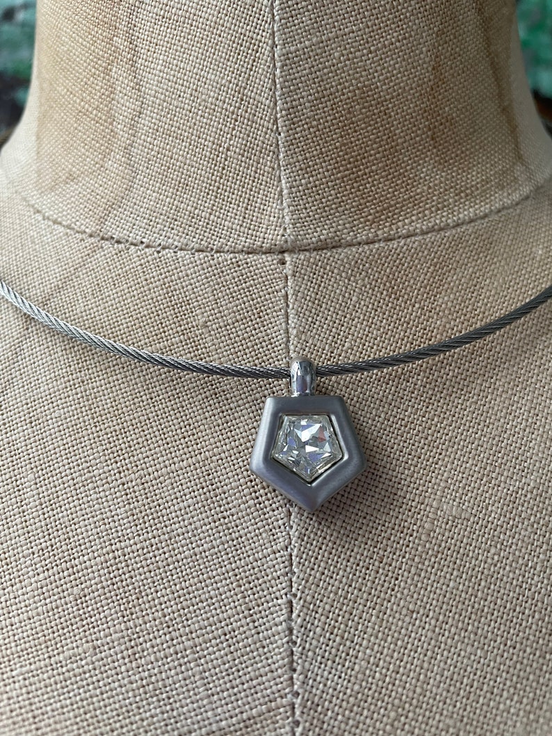 May include: A silver necklace with a geometric pendant featuring a clear crystal.