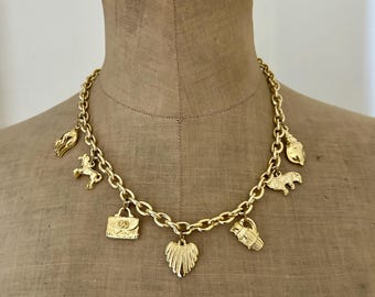 May include: Gold-toned charm necklace featuring various pendants, including a horse, purse, and leaf. The necklace is displayed on a mannequin. The chain is a thick, linked design. The charms are detailed and add visual interest to the jewelry.