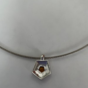 May include: A silver necklace with a pentagon-shaped pendant featuring a small, clear stone in the center.