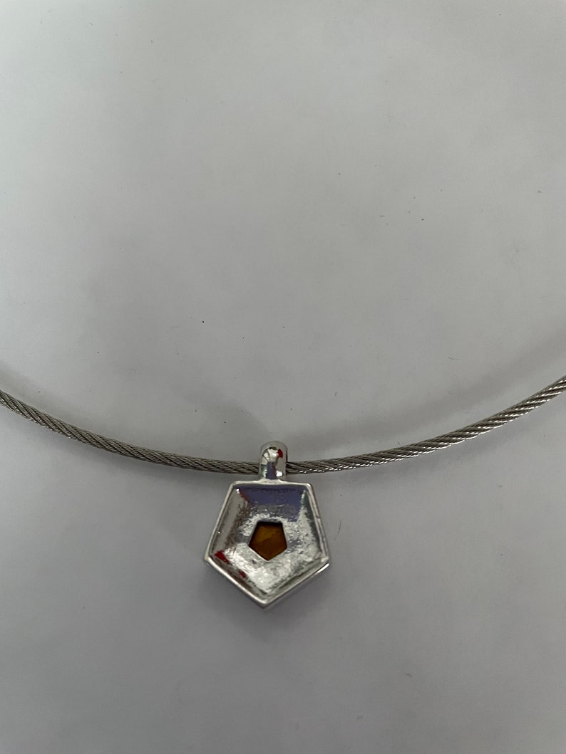 May include: A silver necklace with a pentagon-shaped pendant featuring a small, clear stone in the center.