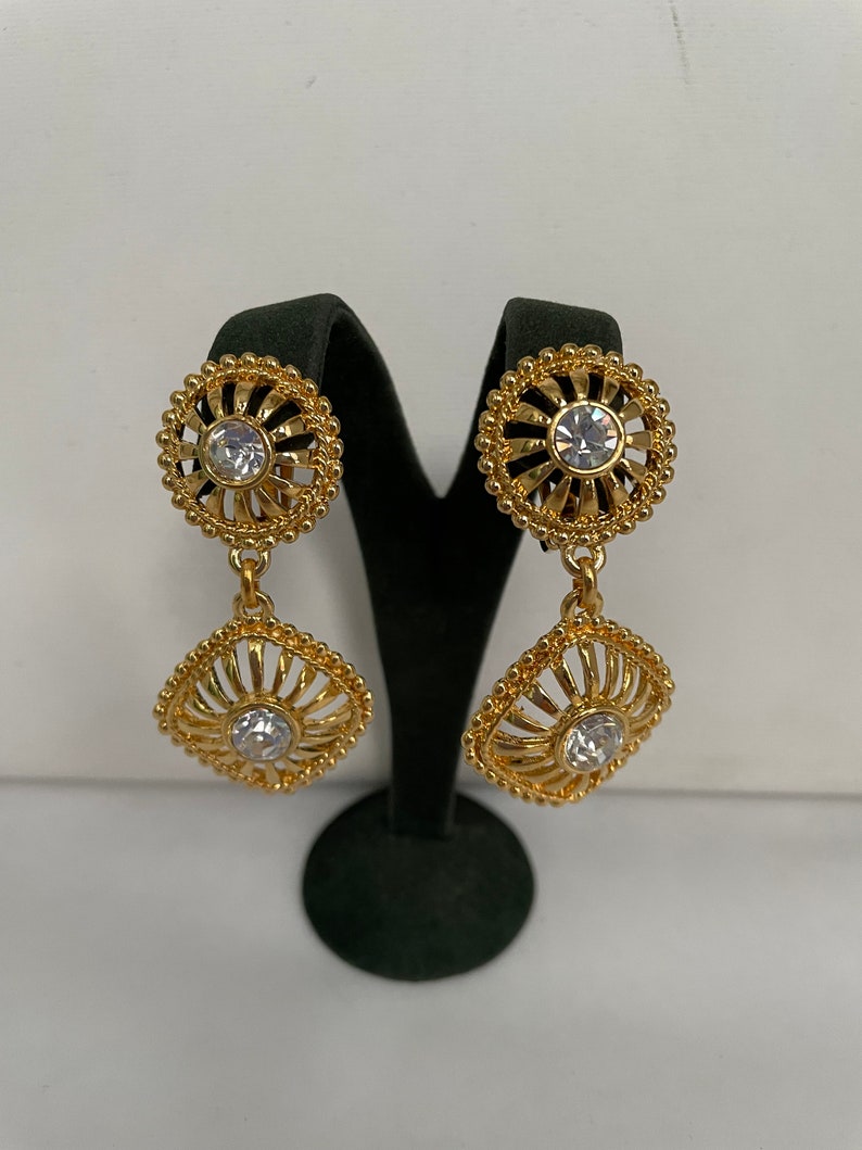 May include: Gold tone dangle earrings with a round and square design featuring clear rhinestones.