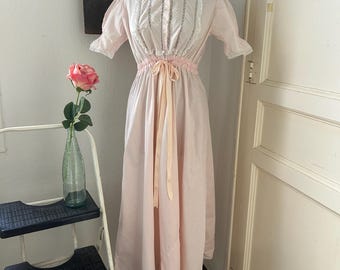 Könnte beinhalten: Ein langes, rosafarbenes, vintage Nachthemd mit weißen Spitzenbesatz und einer Satinband-Schleife an der Taille.