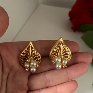 May include: A pair of gold earrings with a delicate, intricate design. Each earring features a cluster of small, white pearls.