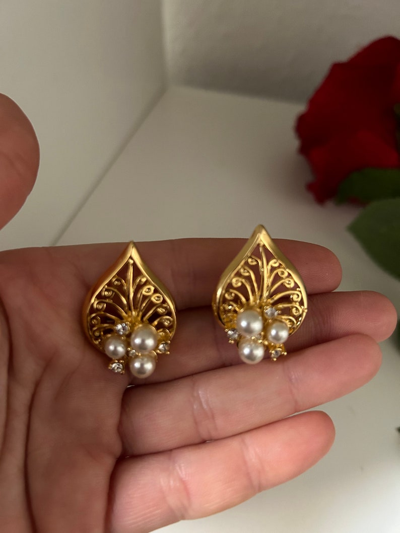 May include: A pair of gold earrings with a delicate, intricate design. Each earring features a cluster of small, white pearls.