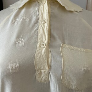 May include: A white cotton shirt with a collar and a button-up front. The shirt has a pocket on the left side and embroidered designs on the front.