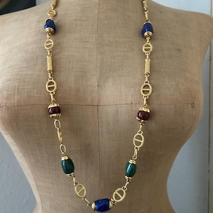 May include: A gold chain necklace with blue, green, and red oval-shaped beads. The chain features a repeating pattern of interlocking circles.