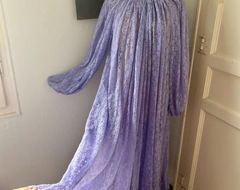 Könnte beinhalten: Ein bodenlanges, lavendelfarbenes Spitzenkleid mit langen, bauschigen Bischofsärmeln, einem gerafften Rundhalsausschnitt mit weißem Saum und einem gerüschten Saum. Der transparente Spitzenstoff mit Blumenmuster fällt locker bis zum Boden.