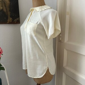 May include: A white short-sleeved blouse with a Peter Pan collar and a single pocket on the left chest.