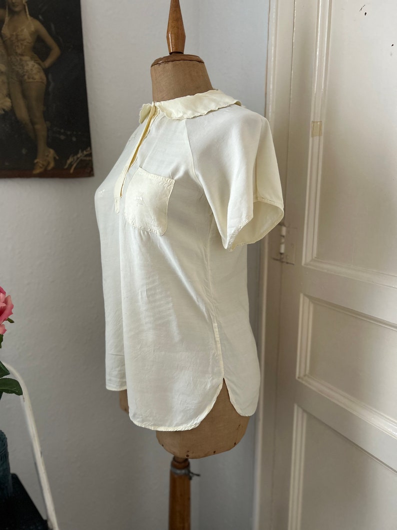 May include: A white short-sleeved blouse with a Peter Pan collar and a single pocket on the left chest.