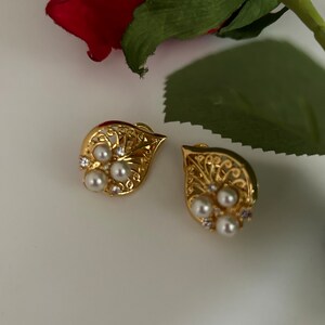 May include: A pair of gold earrings with a delicate filigree design and pearl accents.
