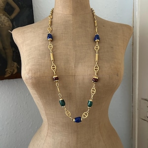 May include: A gold chain necklace with blue, green, and red oval-shaped beads. The chain features a repeating interlocking 'D' design.