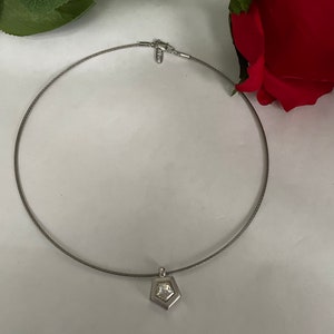 May include: A silver necklace with a pendant featuring a clear crystal set in a geometric shape.