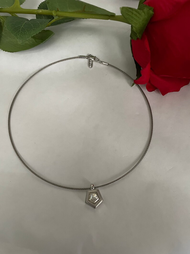 May include: A silver necklace with a pendant featuring a clear crystal set in a geometric shape.