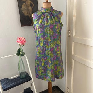 Puede incluir: Un vestido sin mangas con cuello alto y un estampado floral colorido en tonos verdes, morados, rosas y amarillos. El vestido está en un maniquí.